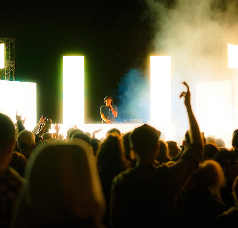 A DJ on stage with bright lights in front of a cheering crowd at Brewloops festival in Kamloops, BC.