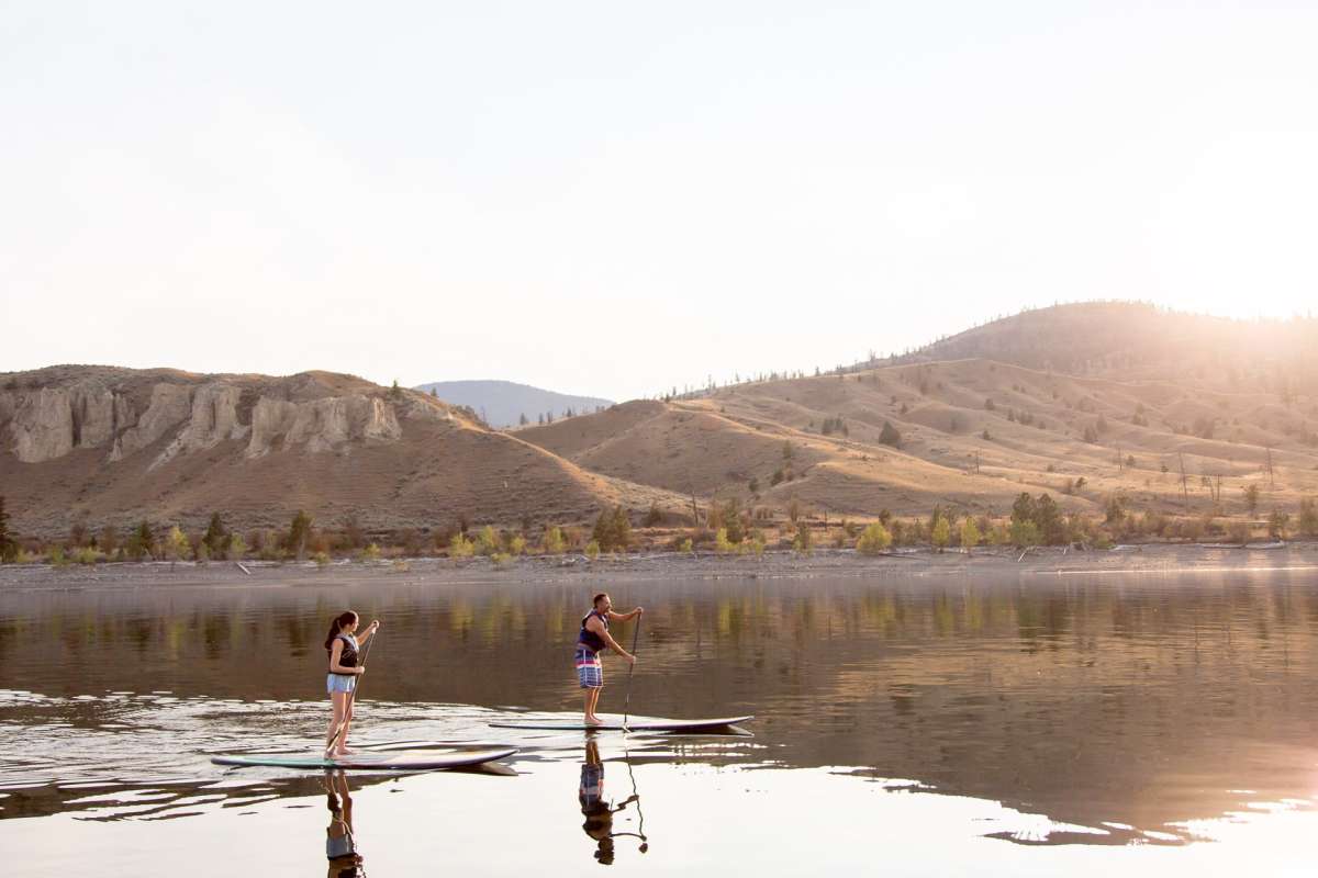 Two paddleboarders on Kamloops Lake surrounded by the natural beauty of the BC mountains in the background.