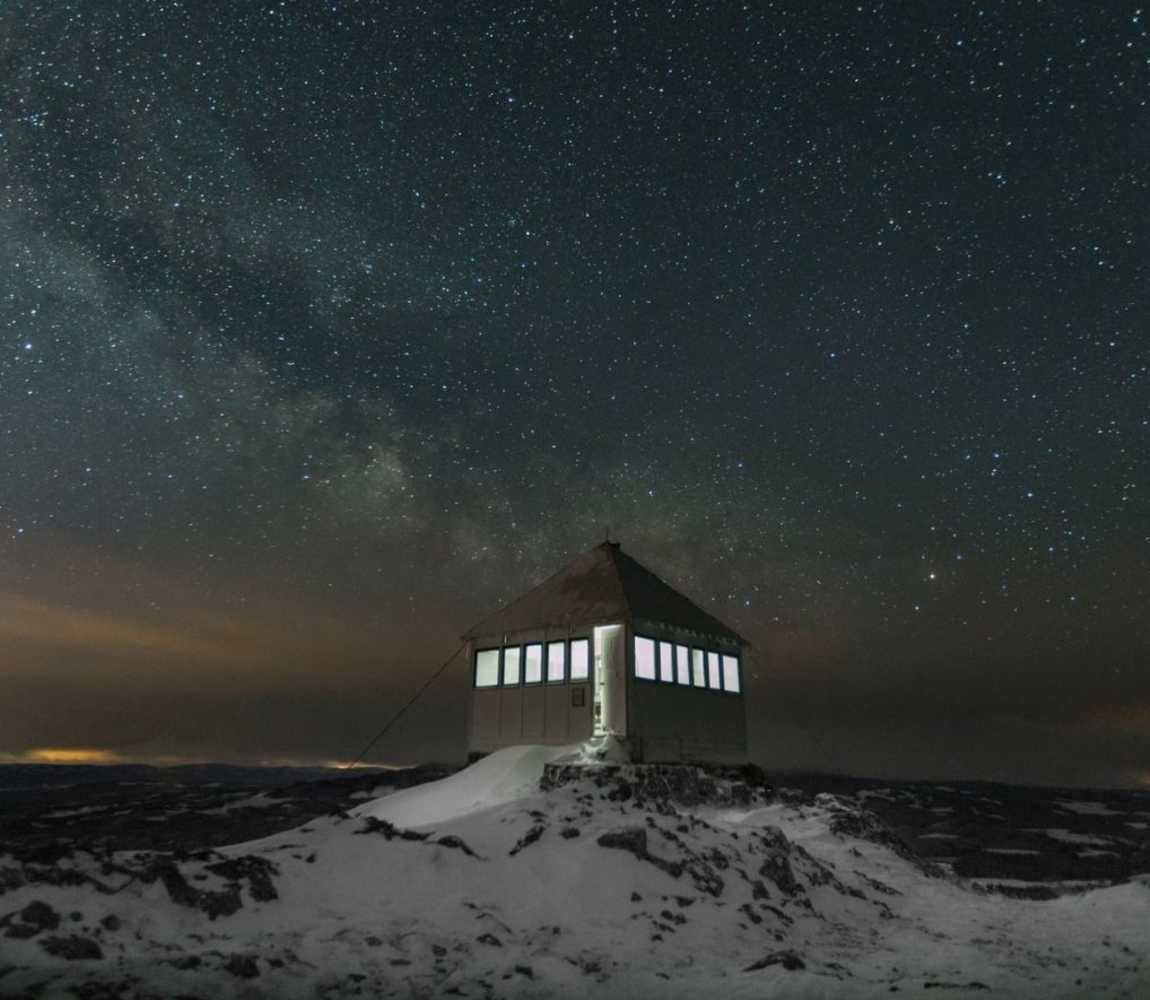 a lit up hut on a snowy mountain under the starry sky