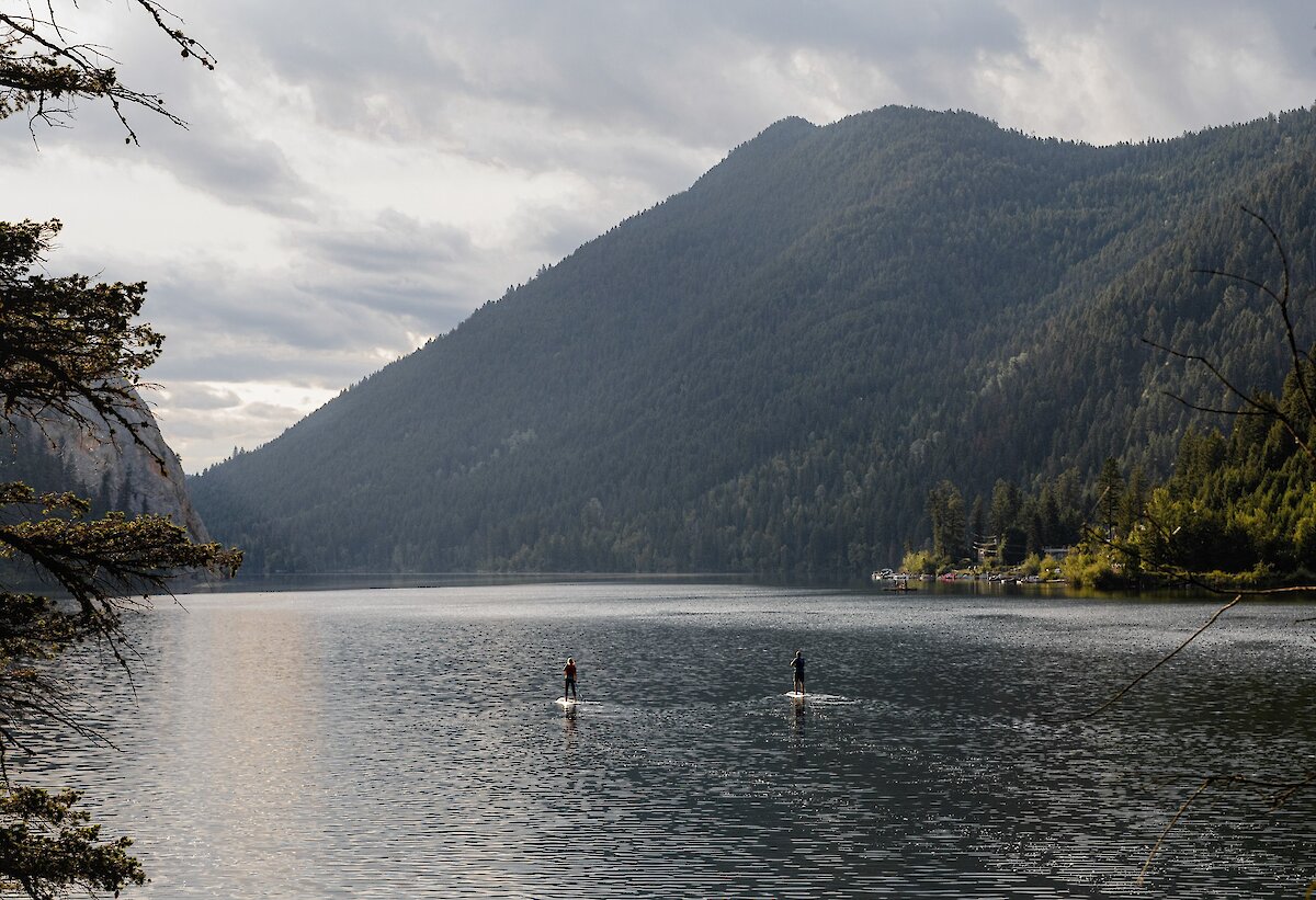 A couple paddleboarding on Paul Lake surrounded by lush greenery located near Kamloops British Columbia.