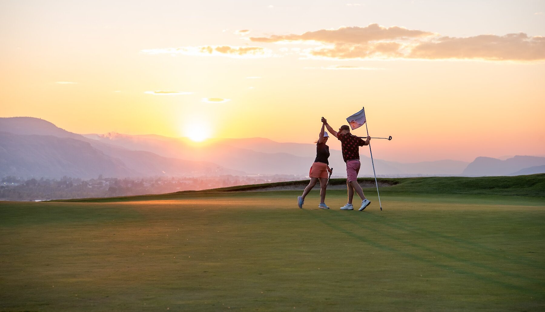Two golfers high-fiving on the golf green with the sunset in the background at the Bighorn Golf & Country Club in Kamloops BC.