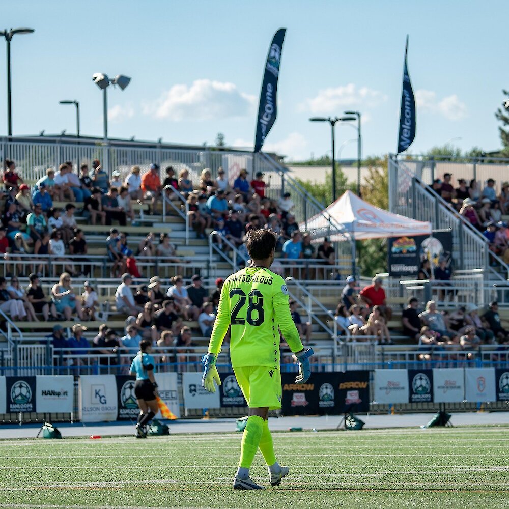 Goalie playing in the Kamloops International Cup walking across the field as Hillside Stadium with the stands full of fans in the background in Kamloops, BC.
