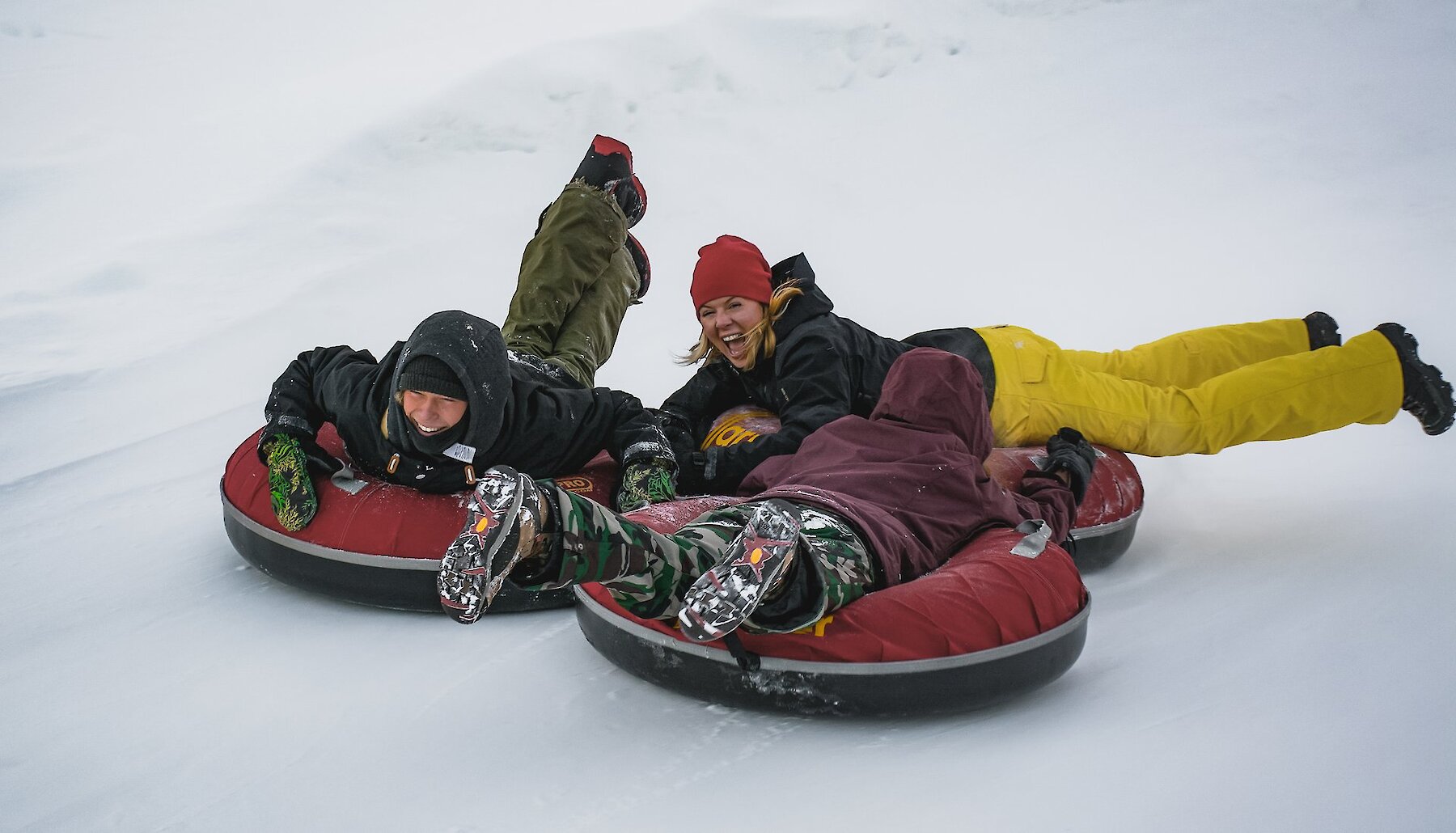 An adult and two children in snow gear laugh as they slide down the tube run at Harper Mountain near Kamloops BC.