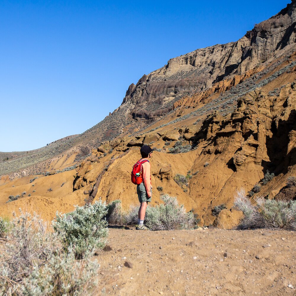 A hiker climbs a steep, narrow chasm between hoodoos.