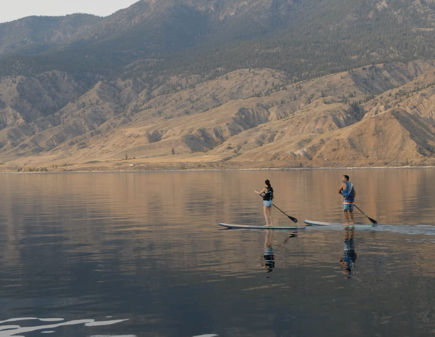 Two paddleboarders gliding across Kamloops Lake with the view of the mountains in the background Kamloops, BC.