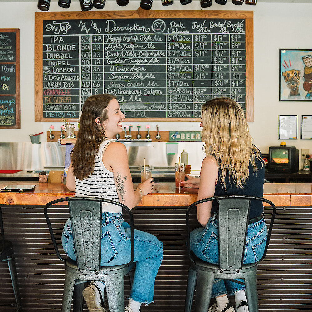 2 girls enjoying drinks at the bar in the Red Collar Brewing Taproom located in Kamloops, BC.