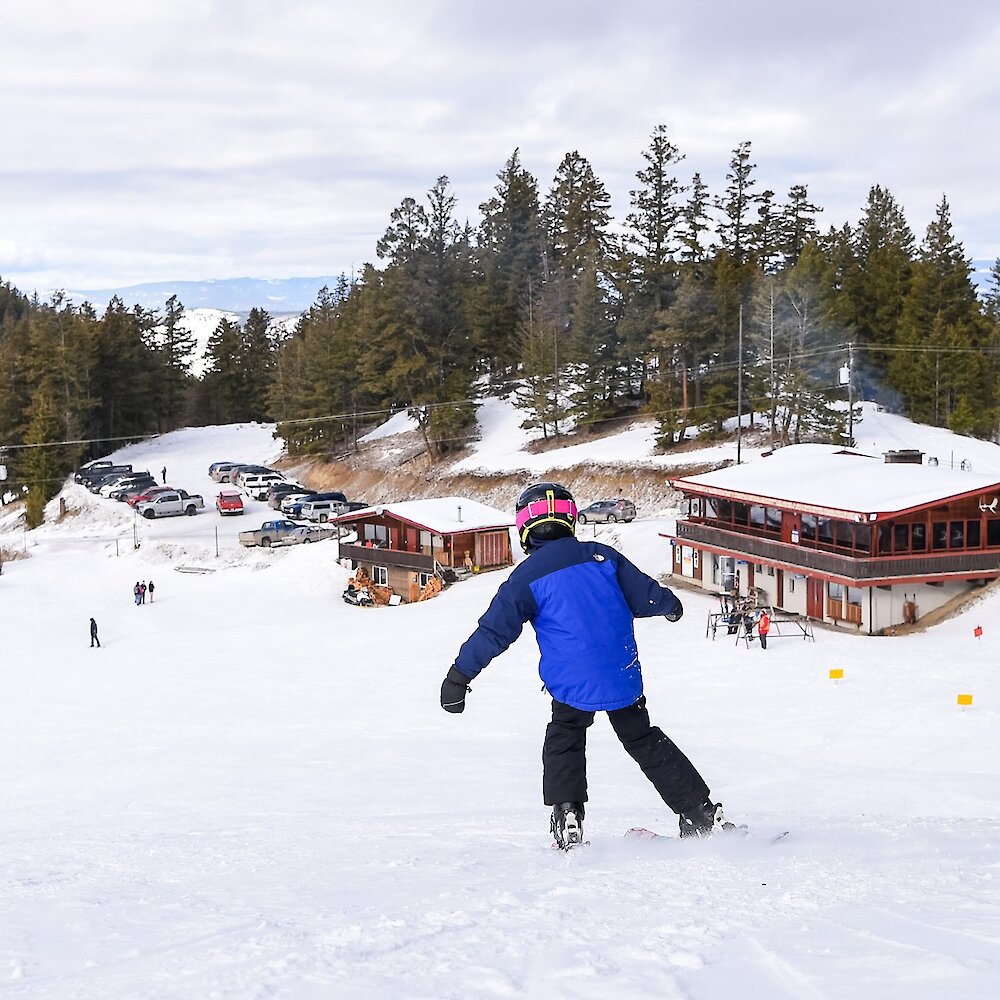 A child skis down the bunny hill at Harper Mountain near Kamloops BC. The lodge is seen in the distance.