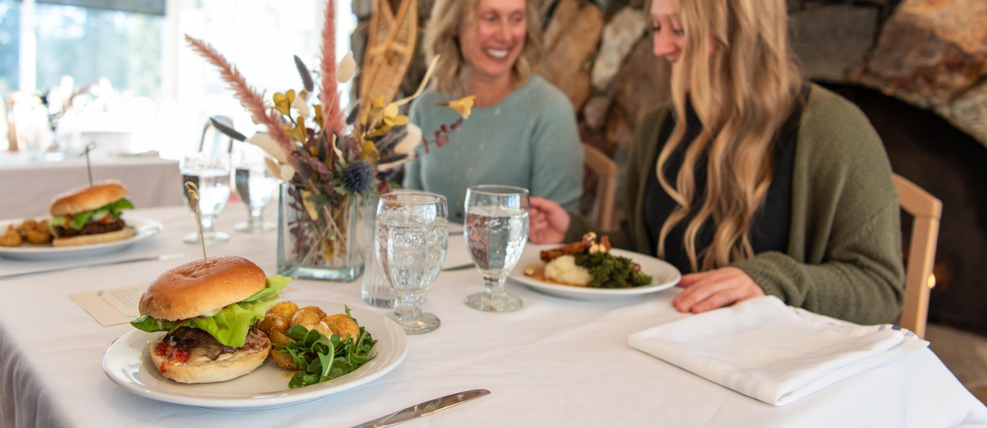 Three women enjoying meals and drinks in a booth at a restaurant.