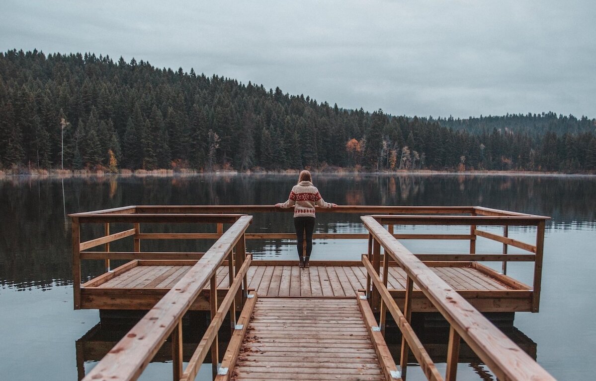 A woman on a dock at Isobel Lake admiring the fall foliage around the shoreline in Kamloops, BC.