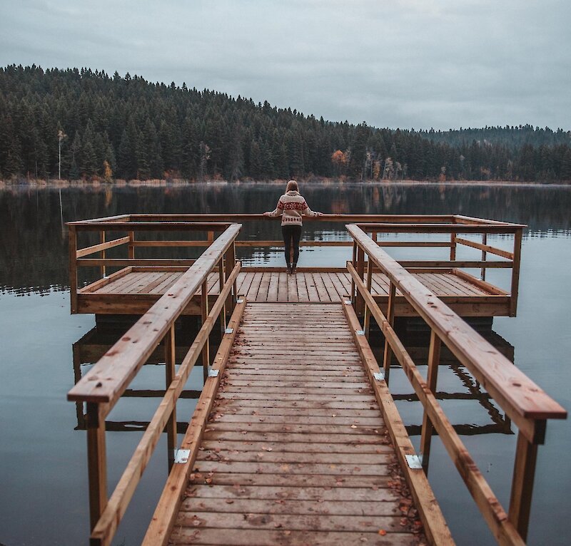 A woman on a dock at Isobel Lake admiring the fall foliage around the shoreline in Kamloops, BC.