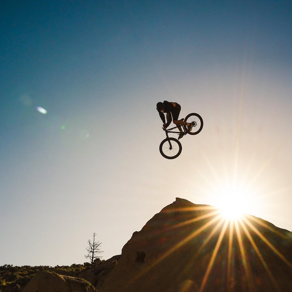 A rider in mid air after taking a jump at the Kamloops Bike Ranch, silhouetted against a sunset.