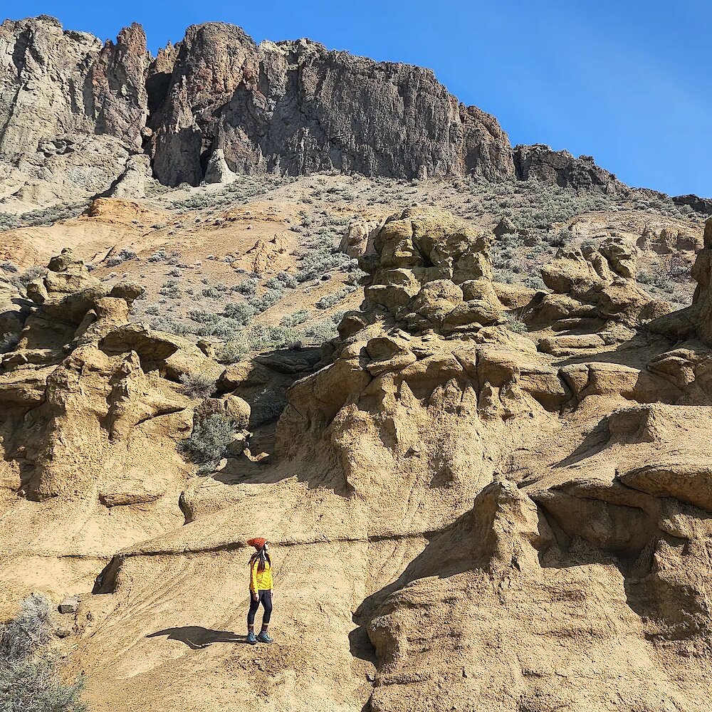 A hiker stands on a slope beneath dramatic hoodoo formations near Kamloops BC.