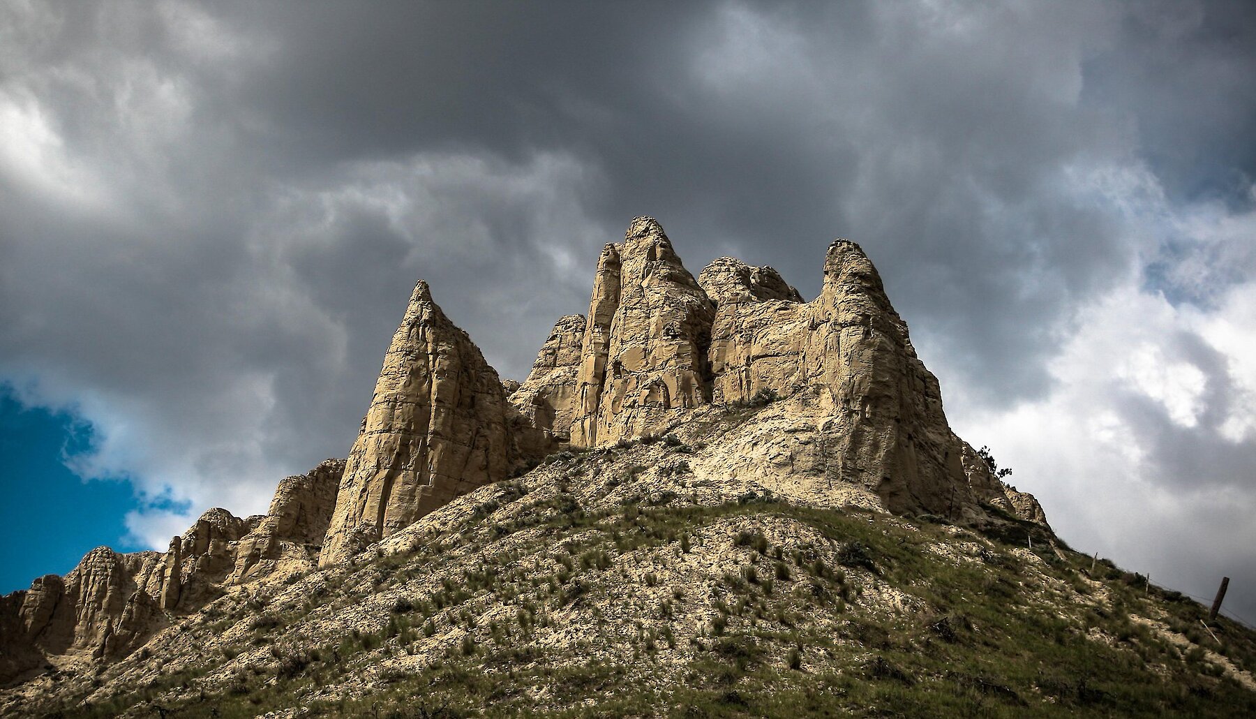 Hoodoos tower against a dramatic cloudy sky in Kamloops BC, with grassland and sagebrush hills in the foreground.