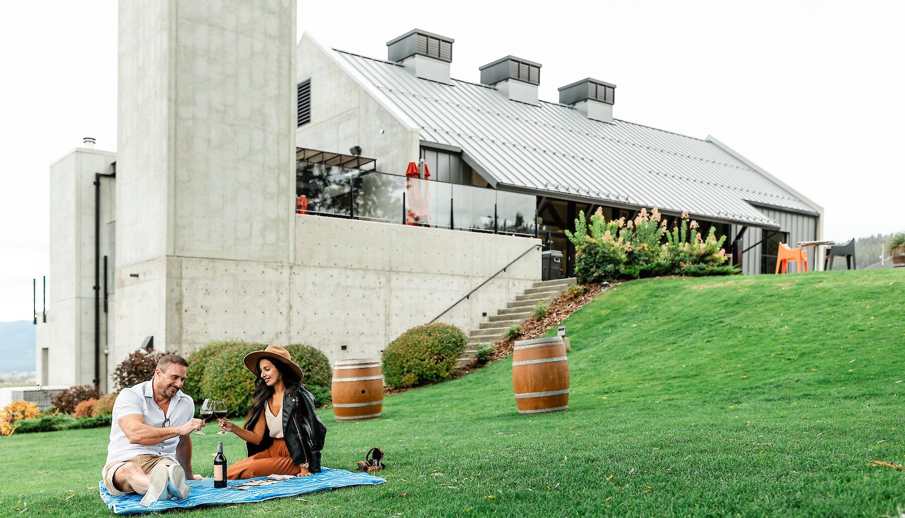 A couple cheers their wine glasses on a picnic blanket on the ground of Monte Creek Winery in Kamloops, BC.
