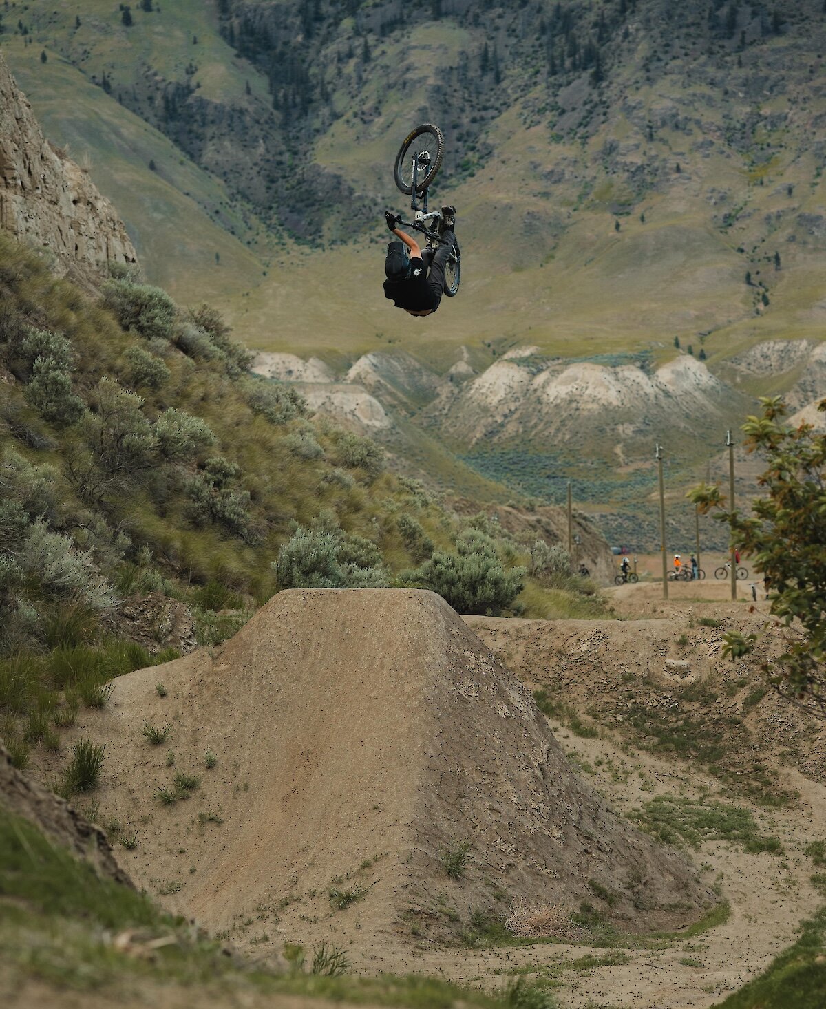 Mountain biker performing a jump with the mountains in the background at the Kamloops Bike Ranch.