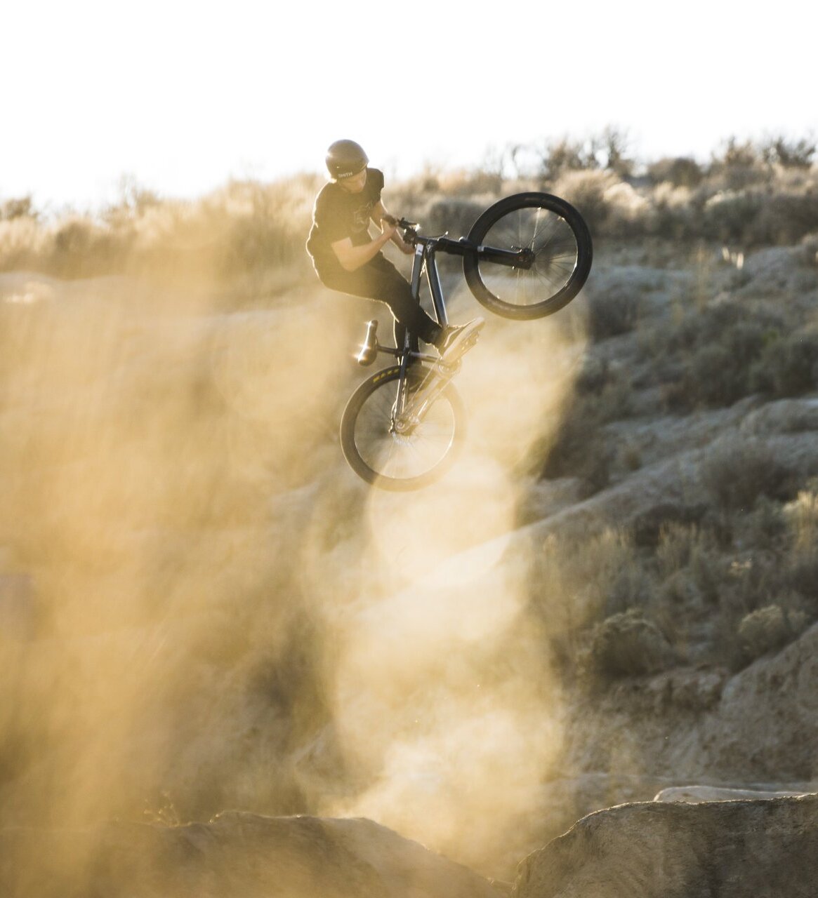 Mountain biker performing a jump with dust cloud.