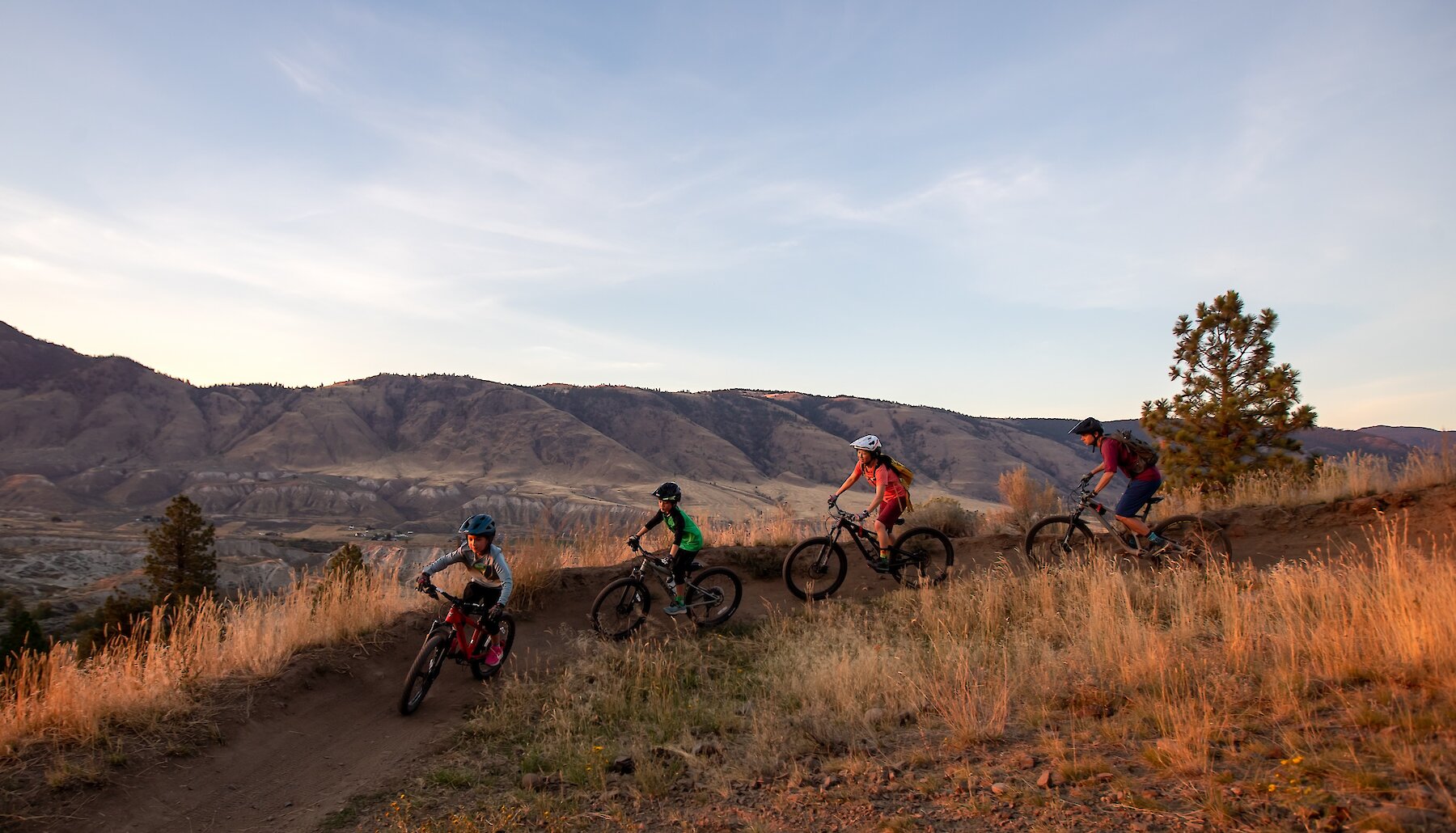 A family mountain bikes down the trail at the Kamloops Bike Ranch with the mountains in the background.