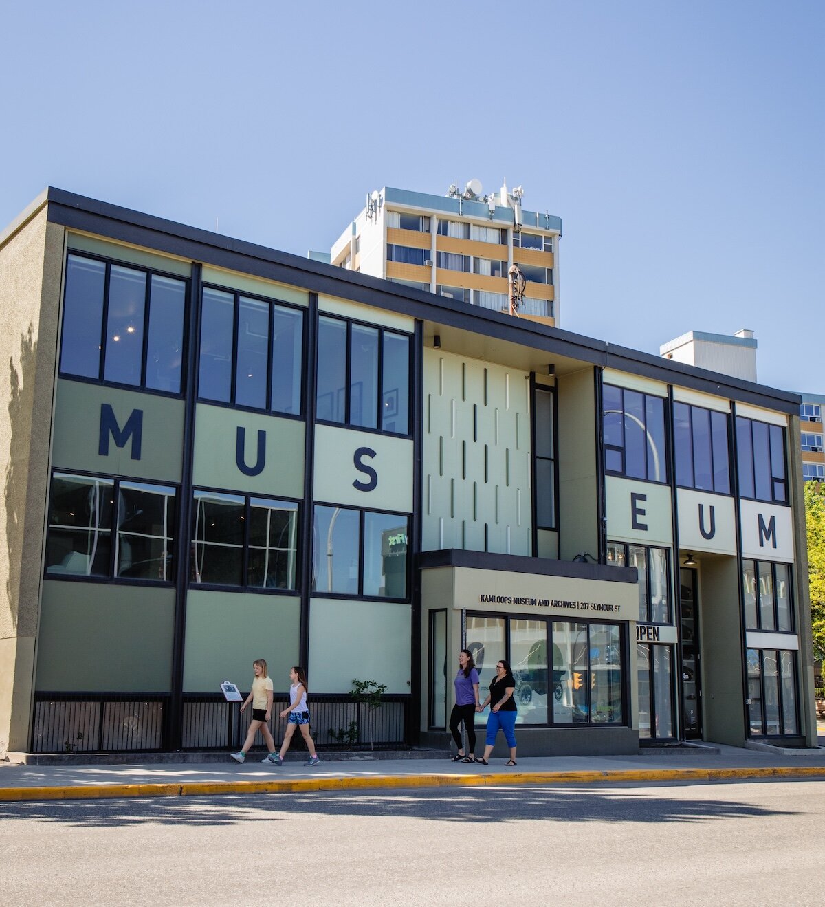 A family walking in front of the Kamloops Museum & Archives on a sunny day in downtown Kamloops, BC.