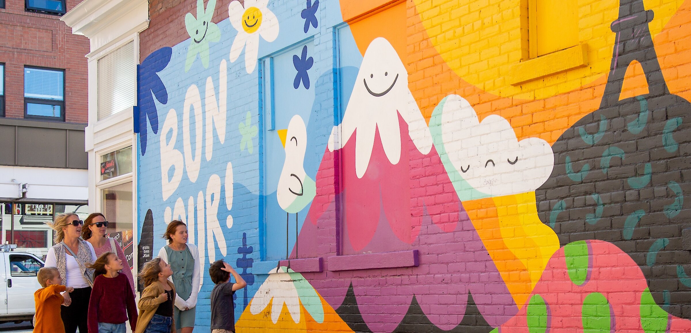 A group of visitors walks along the Bonjour la Francophonie mural looking up at the artwork in downtown Kamloops,BC.