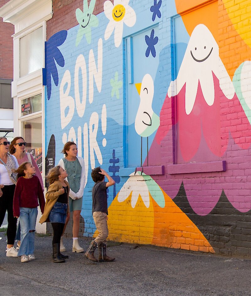 A group of visitors walks along the Bonjour la Francophonie mural looking up at the artwork in downtown Kamloops,BC.