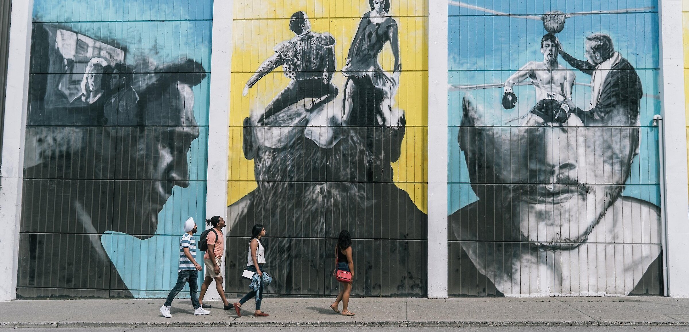 A group of visitors walks along the mural looking up at the artwork in downtown Kamloops,BC.