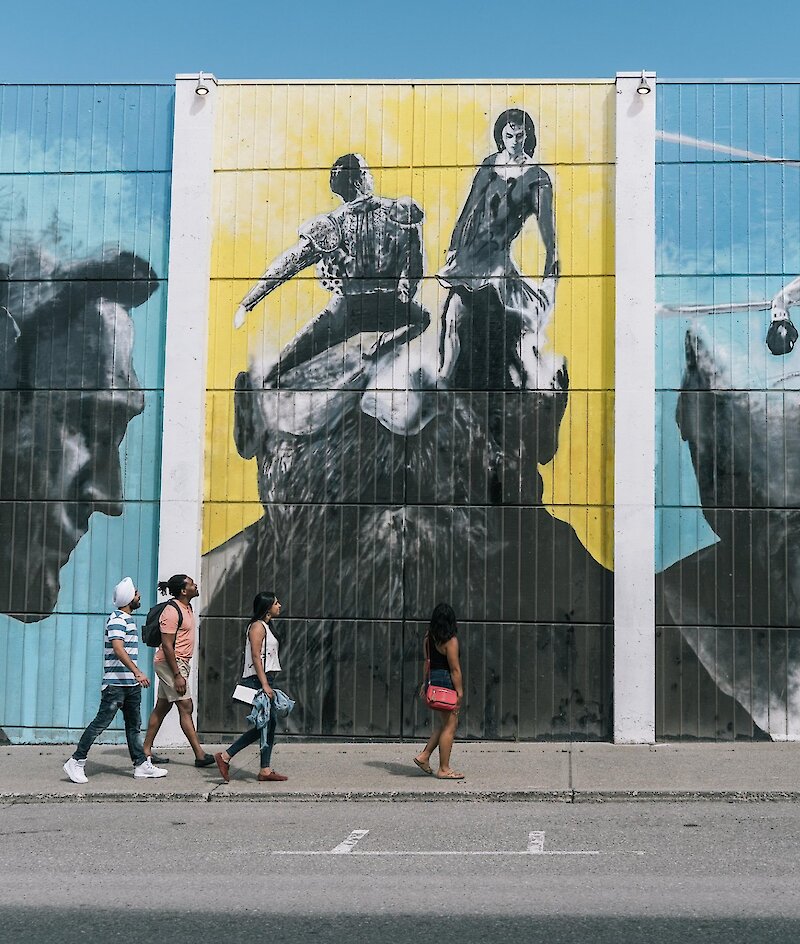 A group of visitors walks along the mural looking up at the artwork in downtown Kamloops,BC.