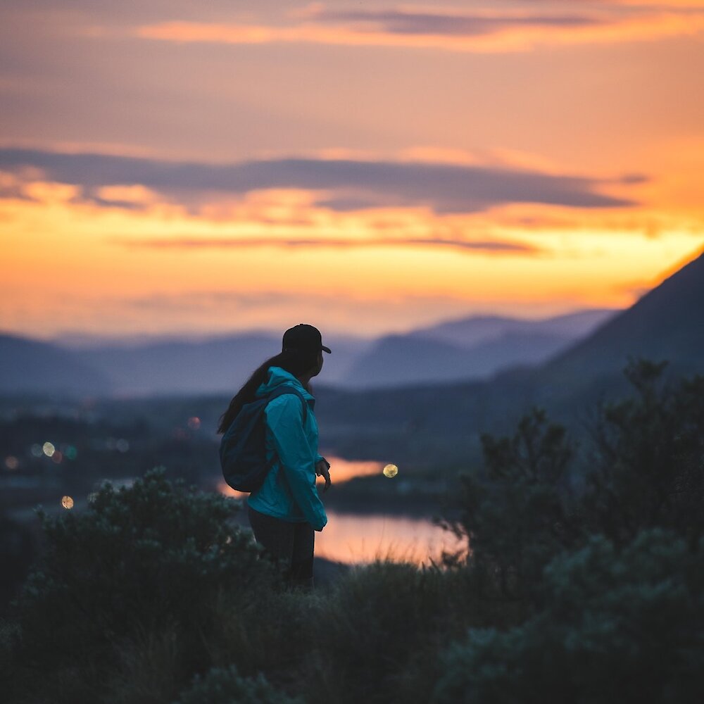 A woman look back over her shoulder at the scenic Kamloops sunset over Kamloops lake and the mountains.