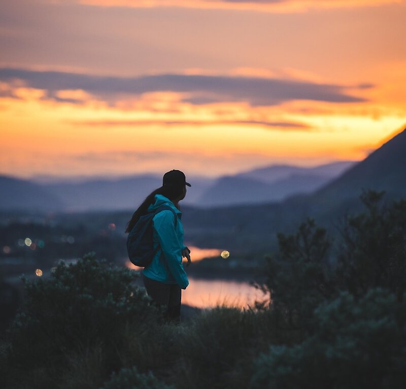 A woman look back over her shoulder at the scenic Kamloops sunset over Kamloops lake and the mountains.