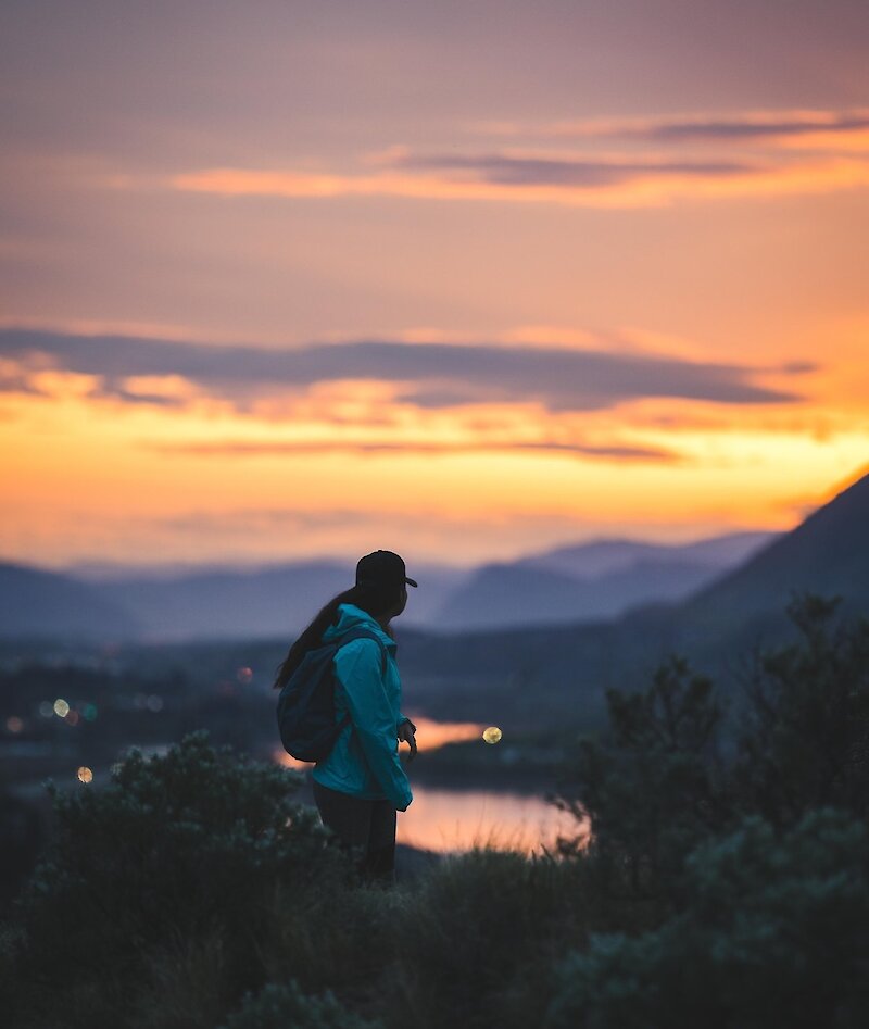 A woman look back over her shoulder at the scenic Kamloops sunset over Kamloops lake and the mountains.