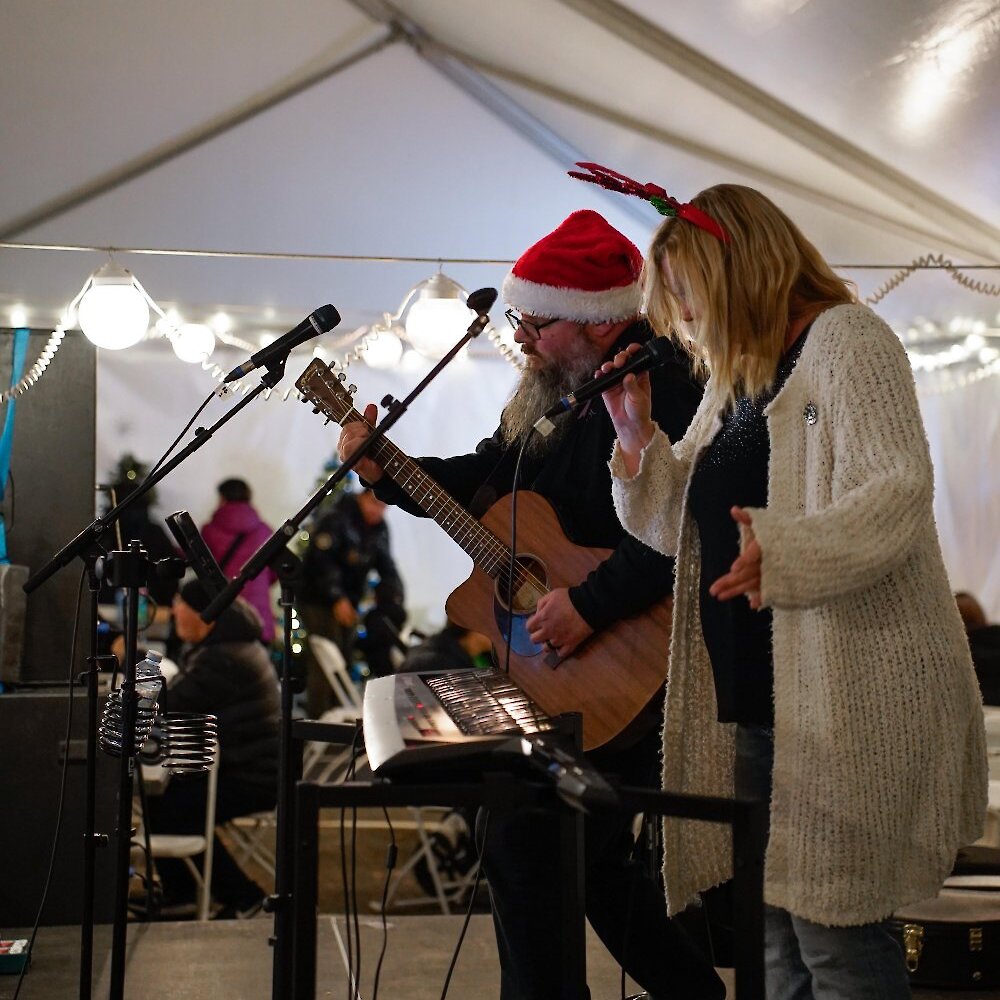 A festive duo in a Santa hat and reindeer antlers performs with guitar, keyboard and vocals on stage at the Kamloops Christmas Market.